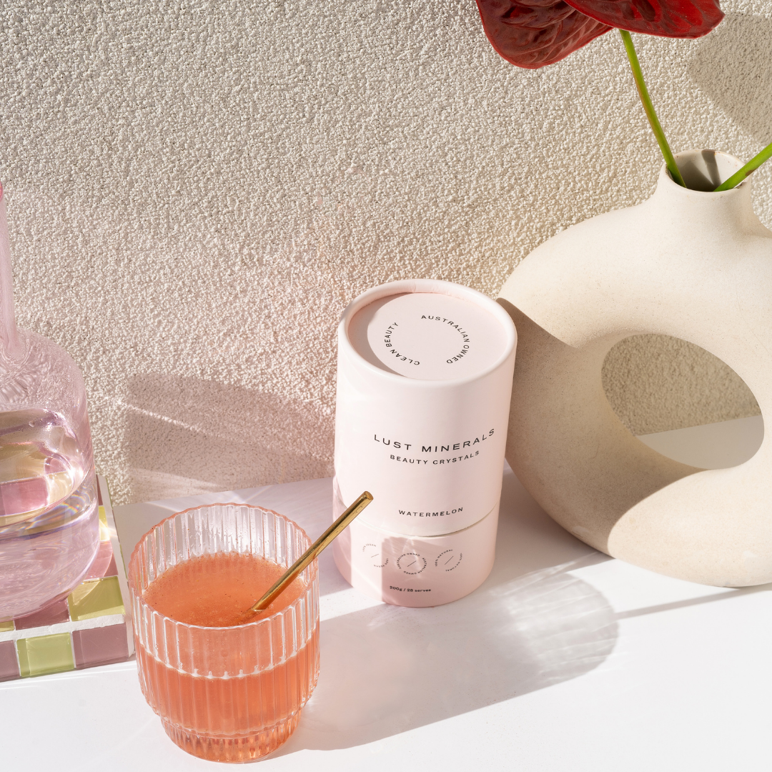 Beauty Crystals next to a glass of pink drink with a straw on a textured surface.
