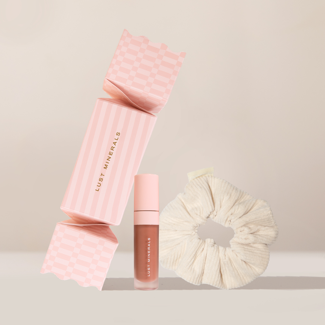 Pink cosmetic case, lipstick, and scrunchie on a beige background