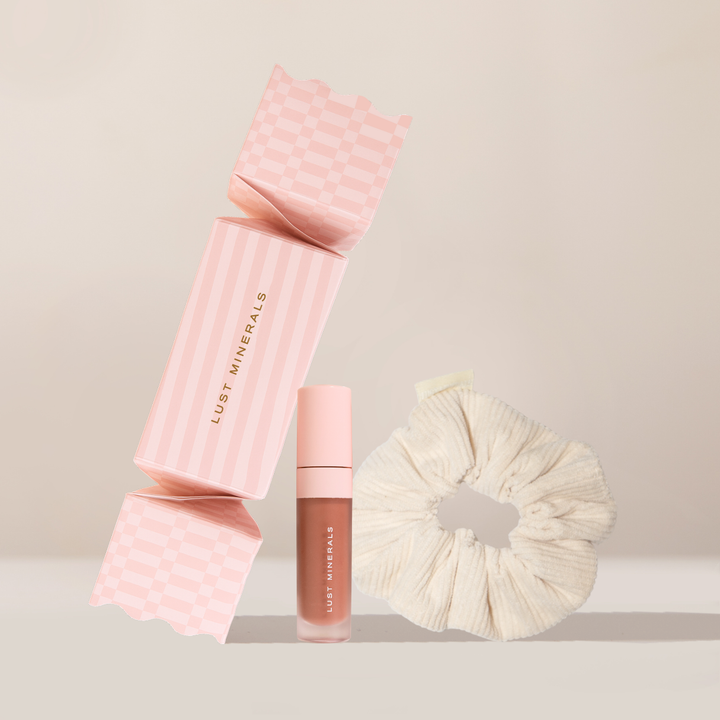 Pink cosmetic case, lipstick, and scrunchie on a beige background