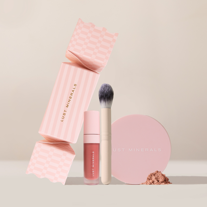 Lust Minerals makeup set with pink packaging, lip product, brush, and powder on a beige background