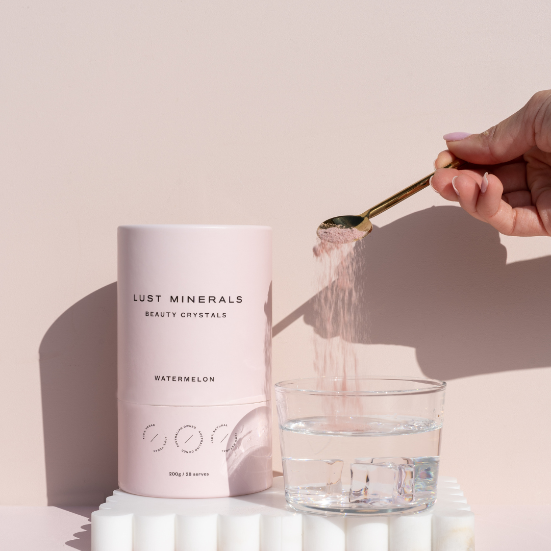 Person adding 'Lust Minerals' beauty crystals to a glass of water on a neutral background