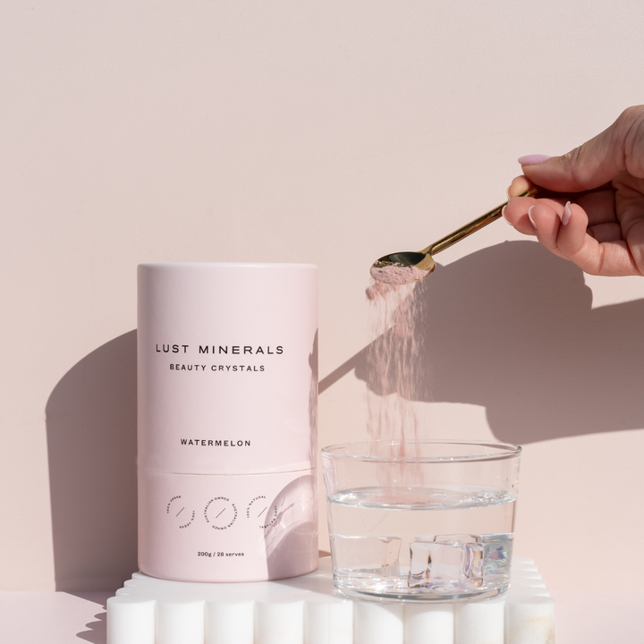 Person adding 'Lust Minerals' beauty crystals to a glass of water on a neutral background